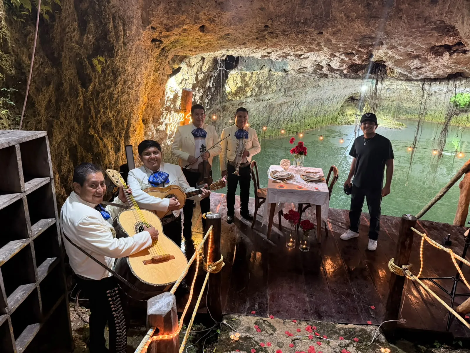 Mariachi tocando junto a una mesa de cena romántica sobre una plataforma de madera dentro de un cenote